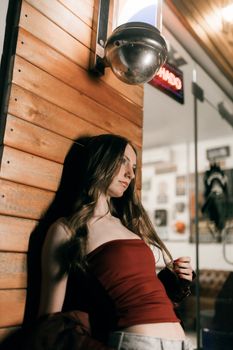 A young woman in a red top leans against a wooden wall, captured at night.