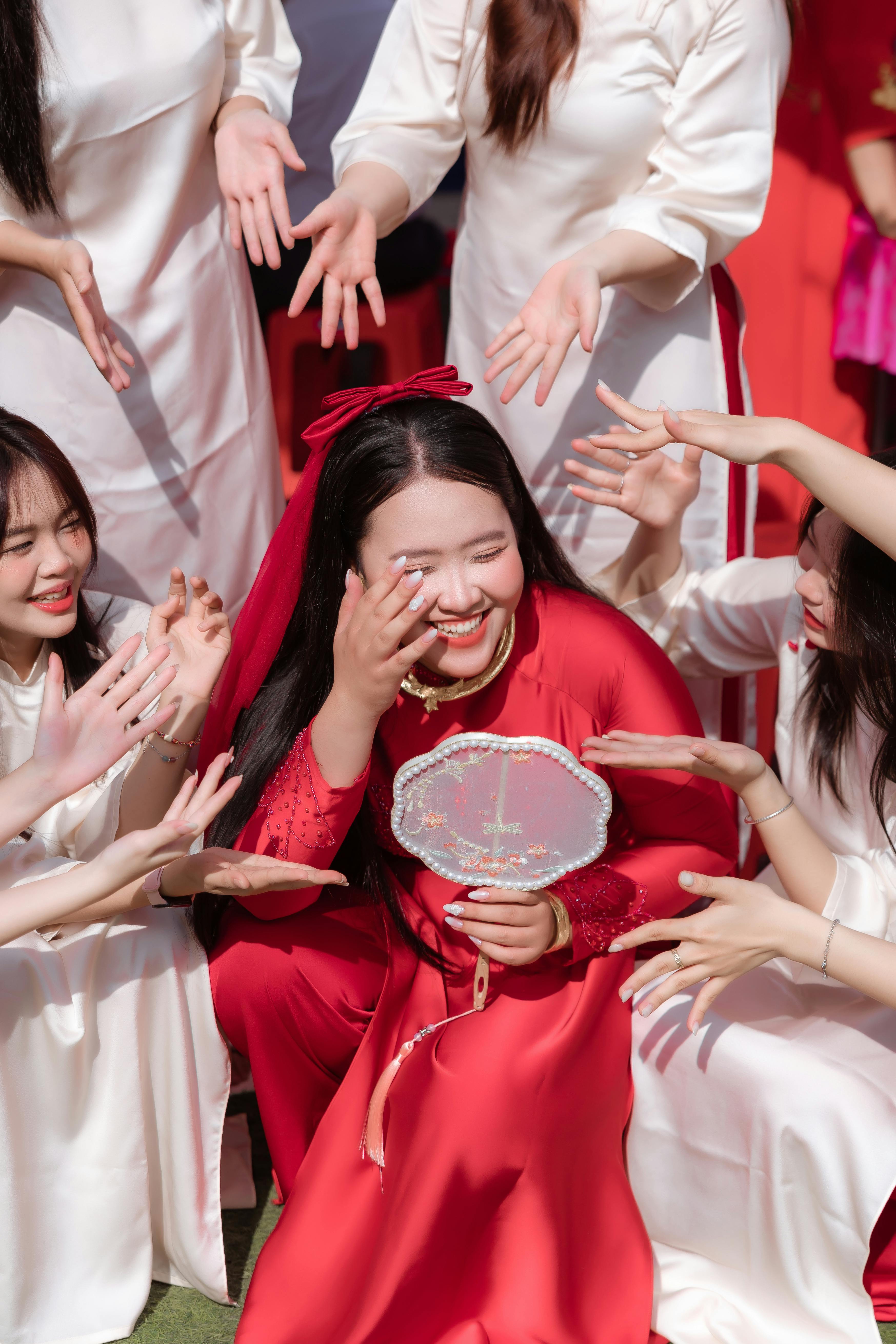 A bride in red surrounded by friends sharing joyous moments on her special day.