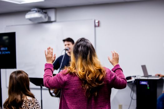 A group of people worshiping indoors, with hands raised, focus on devotion.