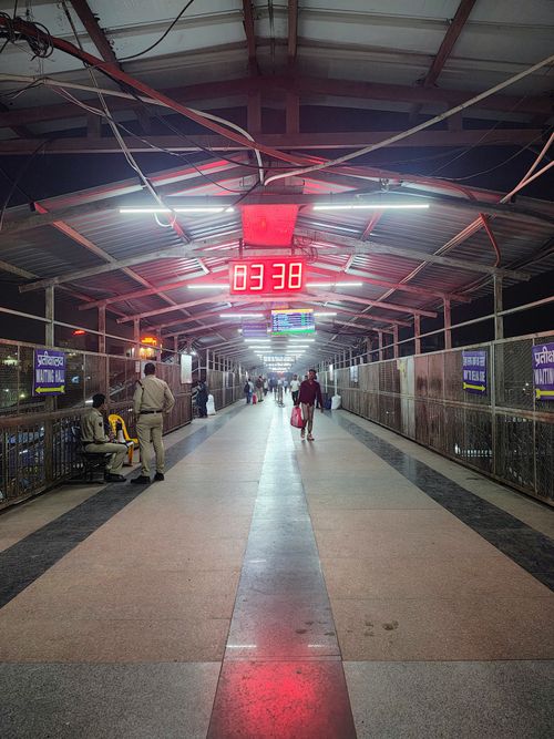 Free A well-lit railway station footbridge bustling with night commuters and security personnel. Stock Photo