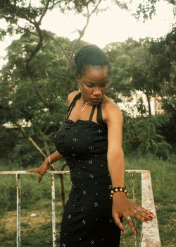 A woman in a stylish black dress poses gracefully outdoors, showcasing elegance and fashion.