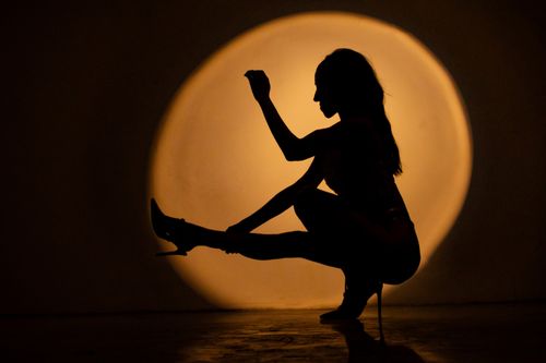 Free Artistic silhouette of a woman posing against a warm circular light, evoking mystery and elegance. Stock Photo