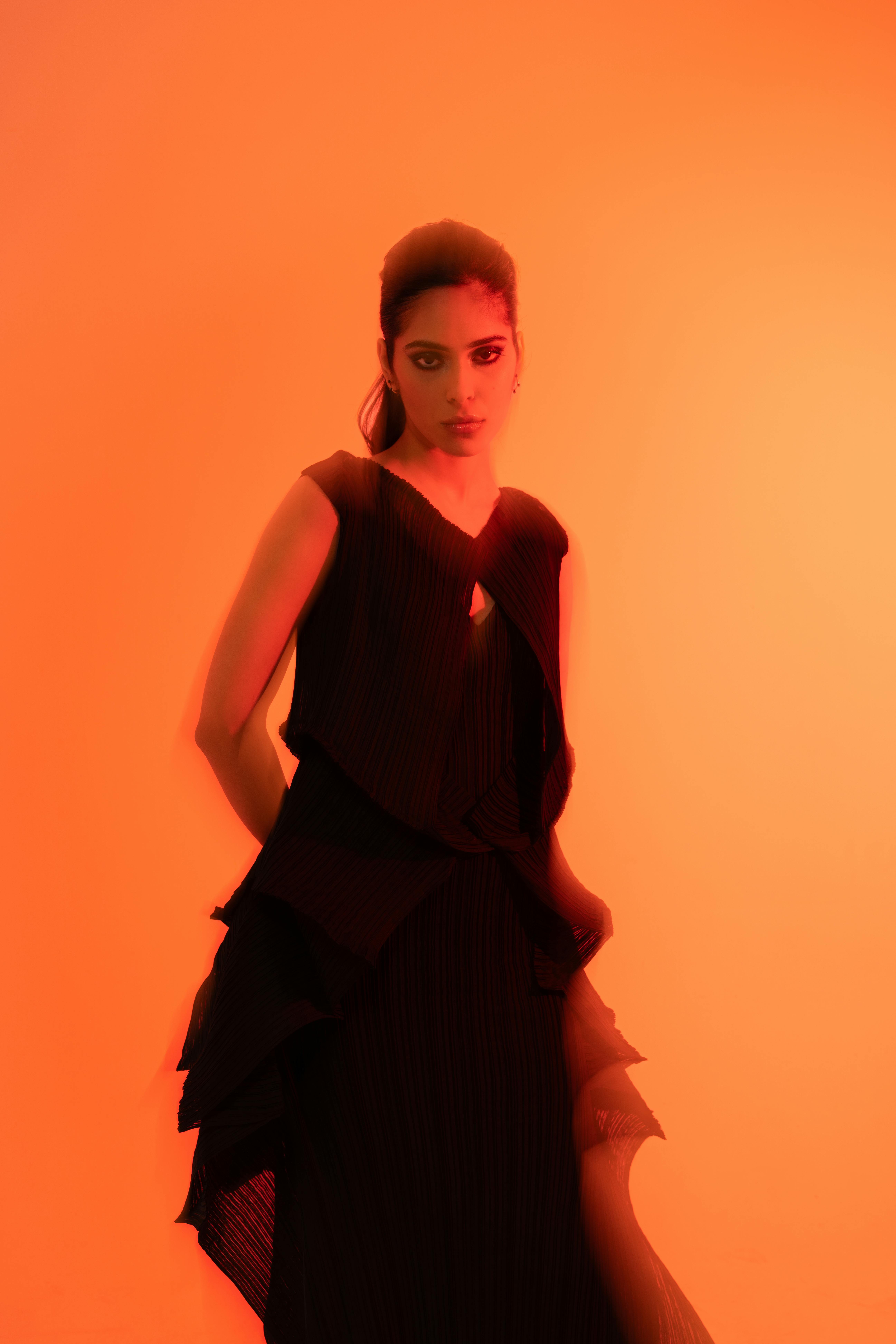 Stylish portrait of a woman in a black dress against a vibrant orange backdrop with artistic motion blur.