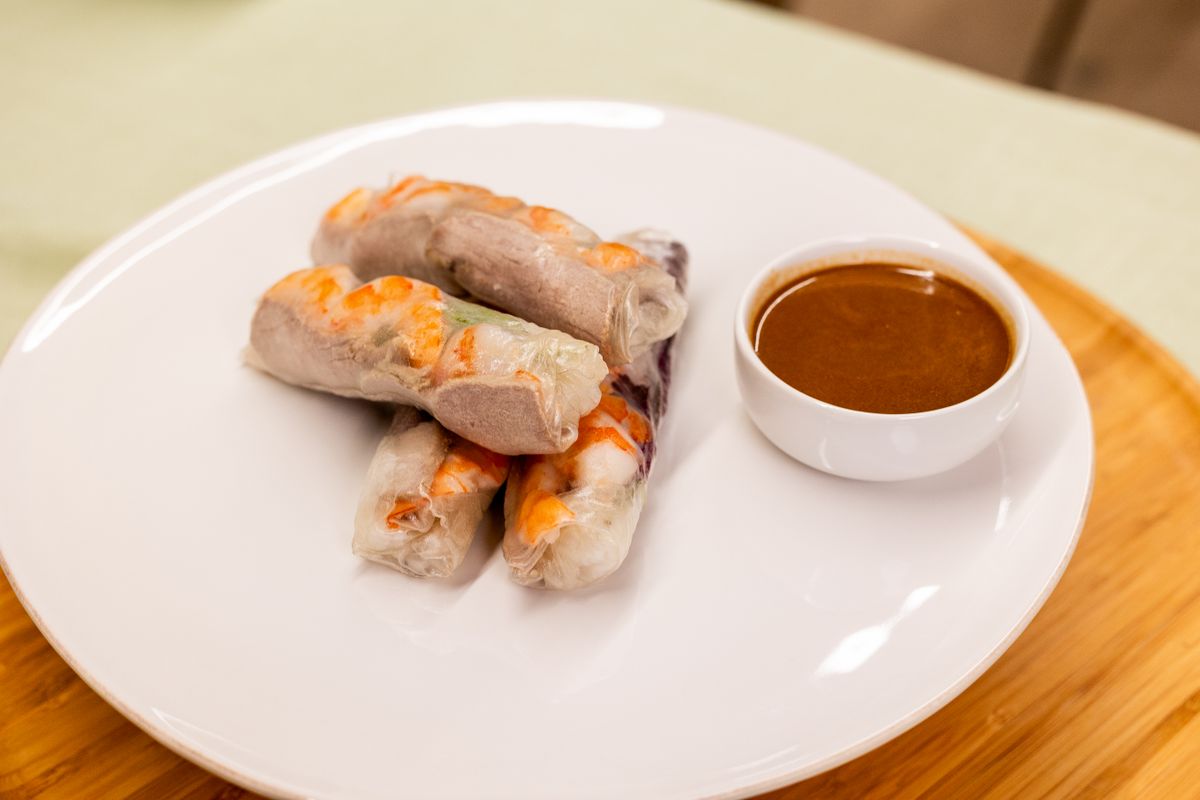 Rice paper rolls showing pink shrimp and sliced pork beside a small bowl of peanut sauce