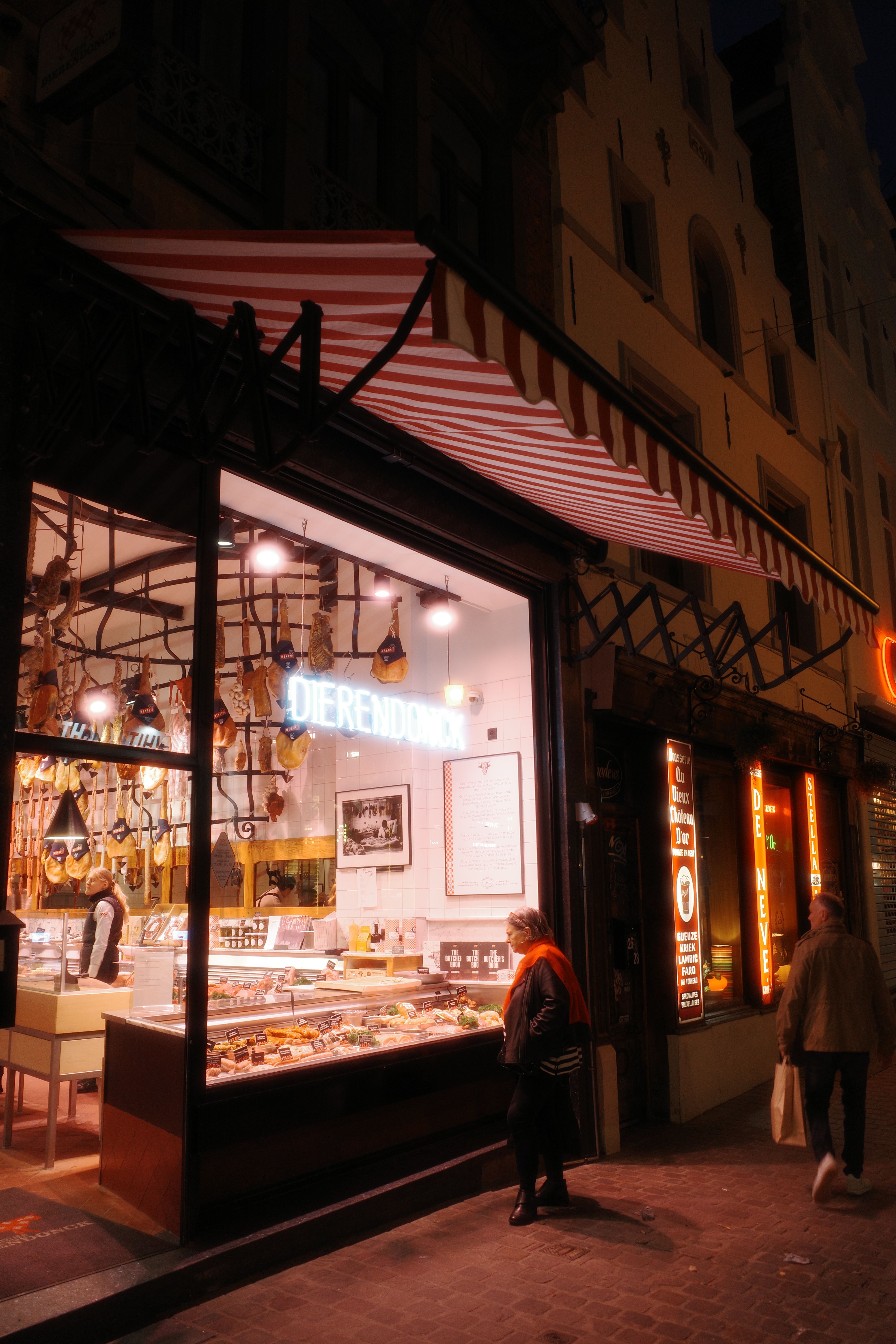 Night view of people outside a deli in Brussels, showcasing a vibrant food display.