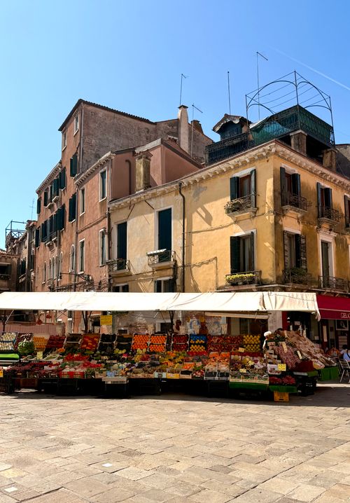 Free Colorful fruit and vegetable stall set against historic Italian architecture on a sunny day. Stock Photo