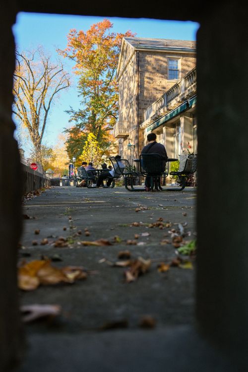 Free Autumn shot of people enjoying outdoor café with fall foliage, framed by stone opening. Stock Photo