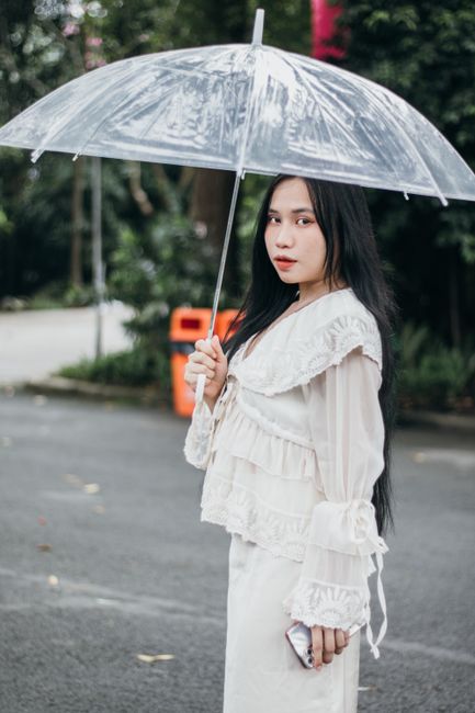 Stylish woman in a white dress holding a transparent umbrella outdoors.