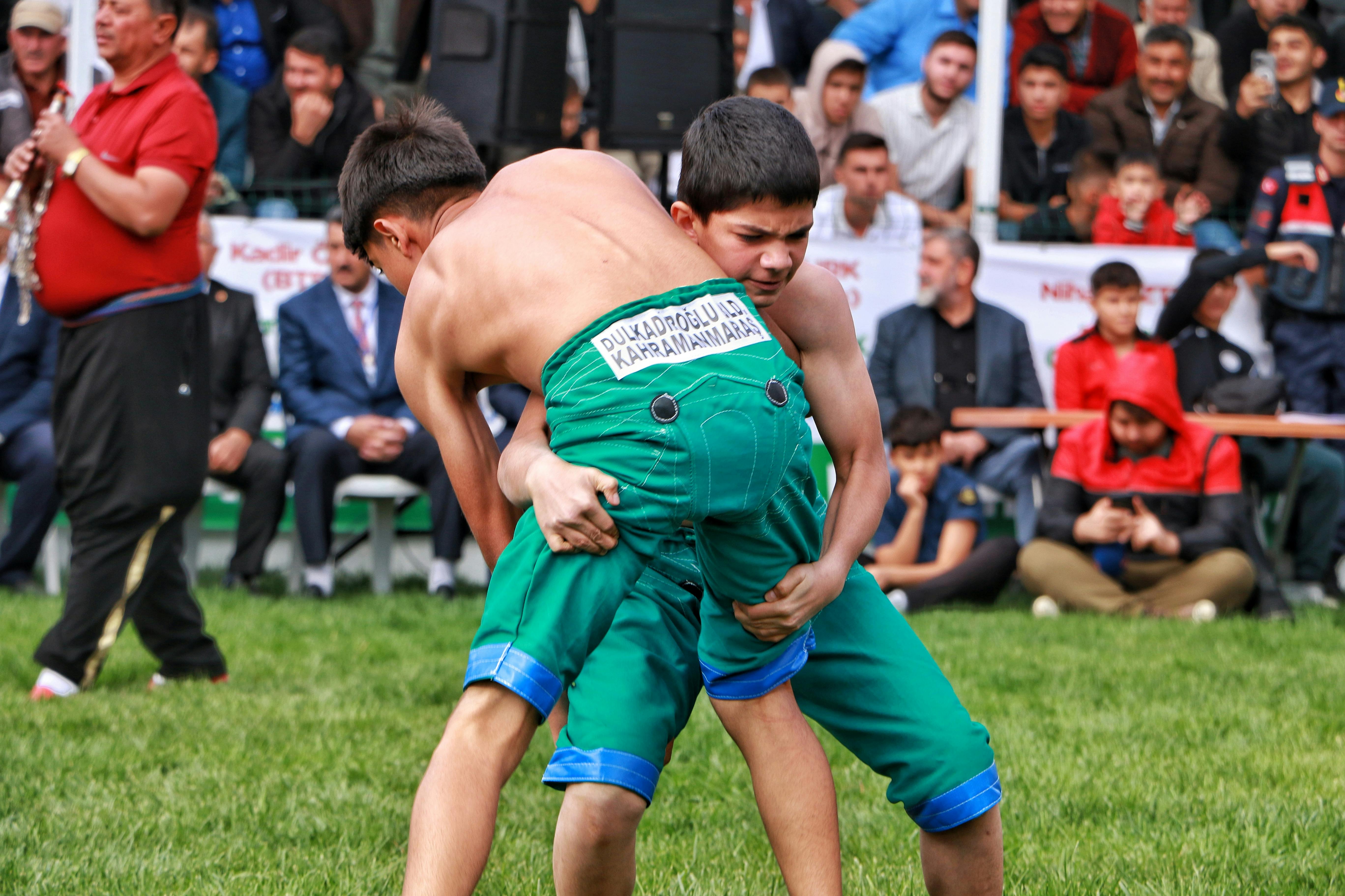 Two young athletes compete in a traditional Turkish oil wrestling match outdoors.