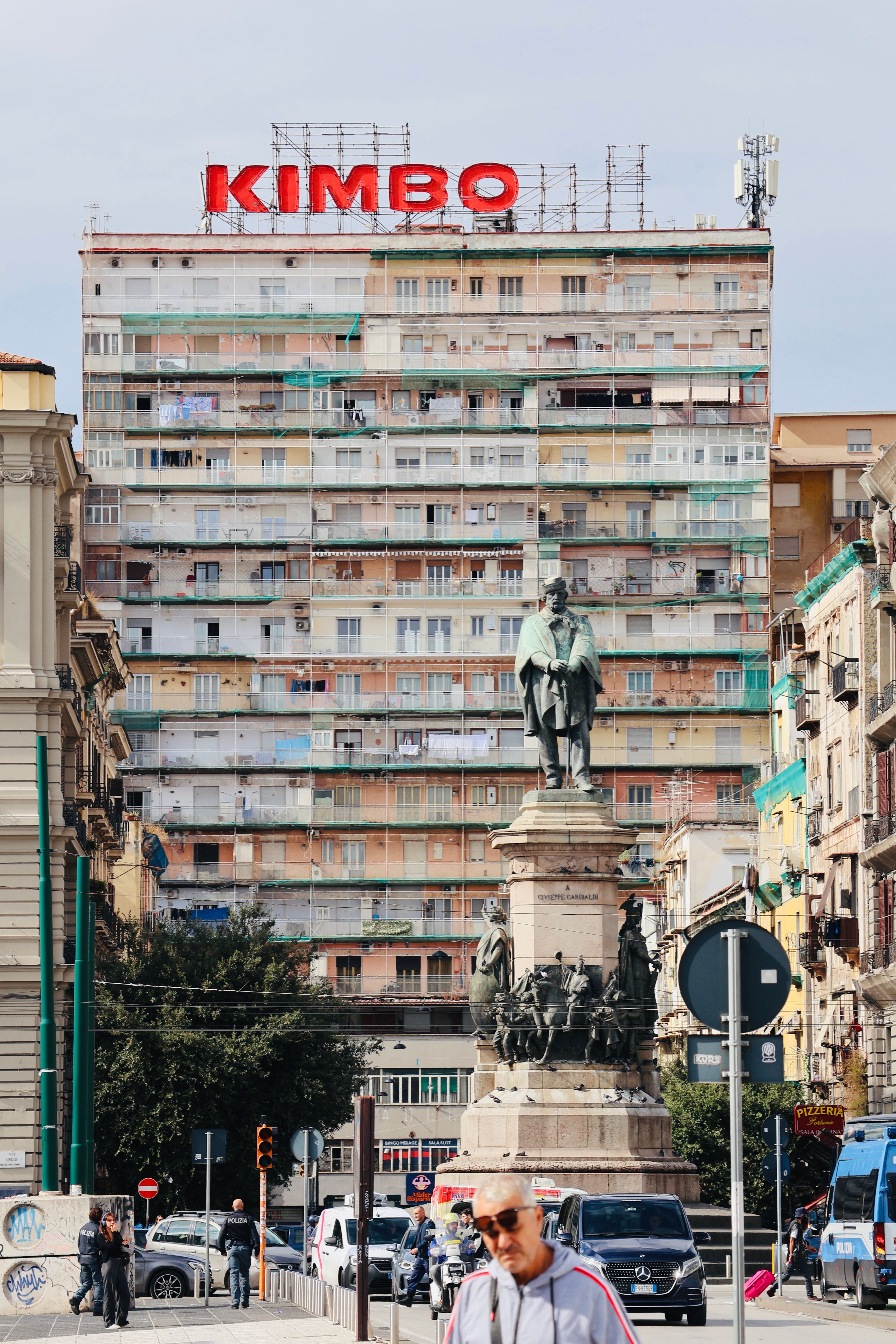 A city intersection with a historic monument, busy street, and apartment building in the background.