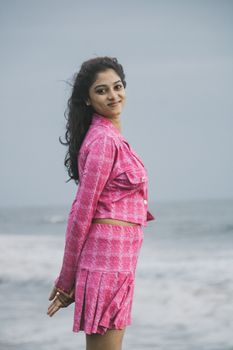 Woman in a pink outfit poses by the seaside, exuding style and grace.
