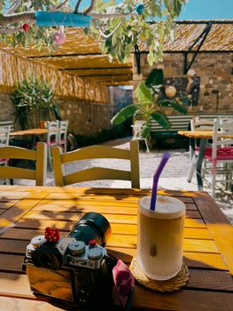 Enjoying a sunny day at an outdoor cafe with iced coffee and camera on a rustic table.