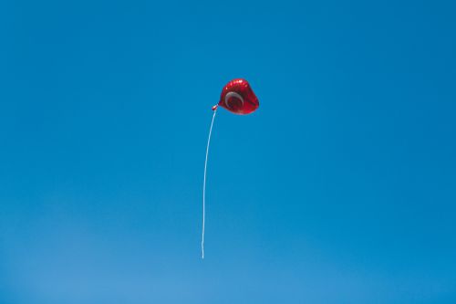 Free A red heart-shaped balloon floating freely in a vibrant blue sky, symbolizing freedom or love. Stock Photo