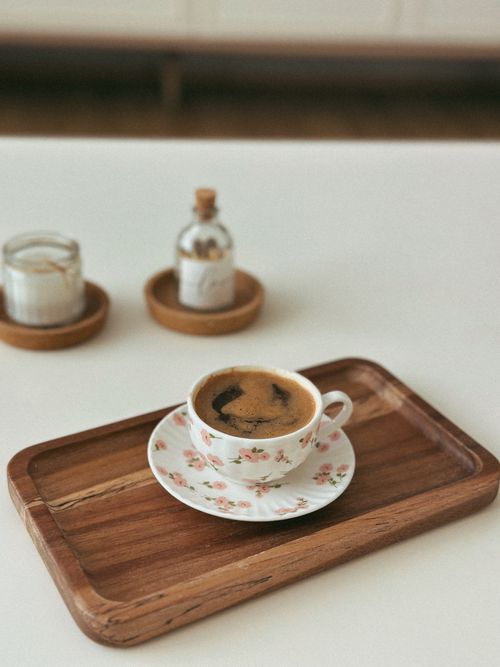 Free Floral coffee cup on wooden tray with candle and bottle, perfect for cozy mornings. Stock Photo