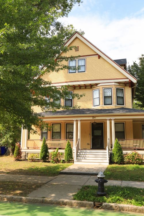 Free A beautiful yellow Victorian-style house with lush greenery and a welcoming porch. Stock Photo
