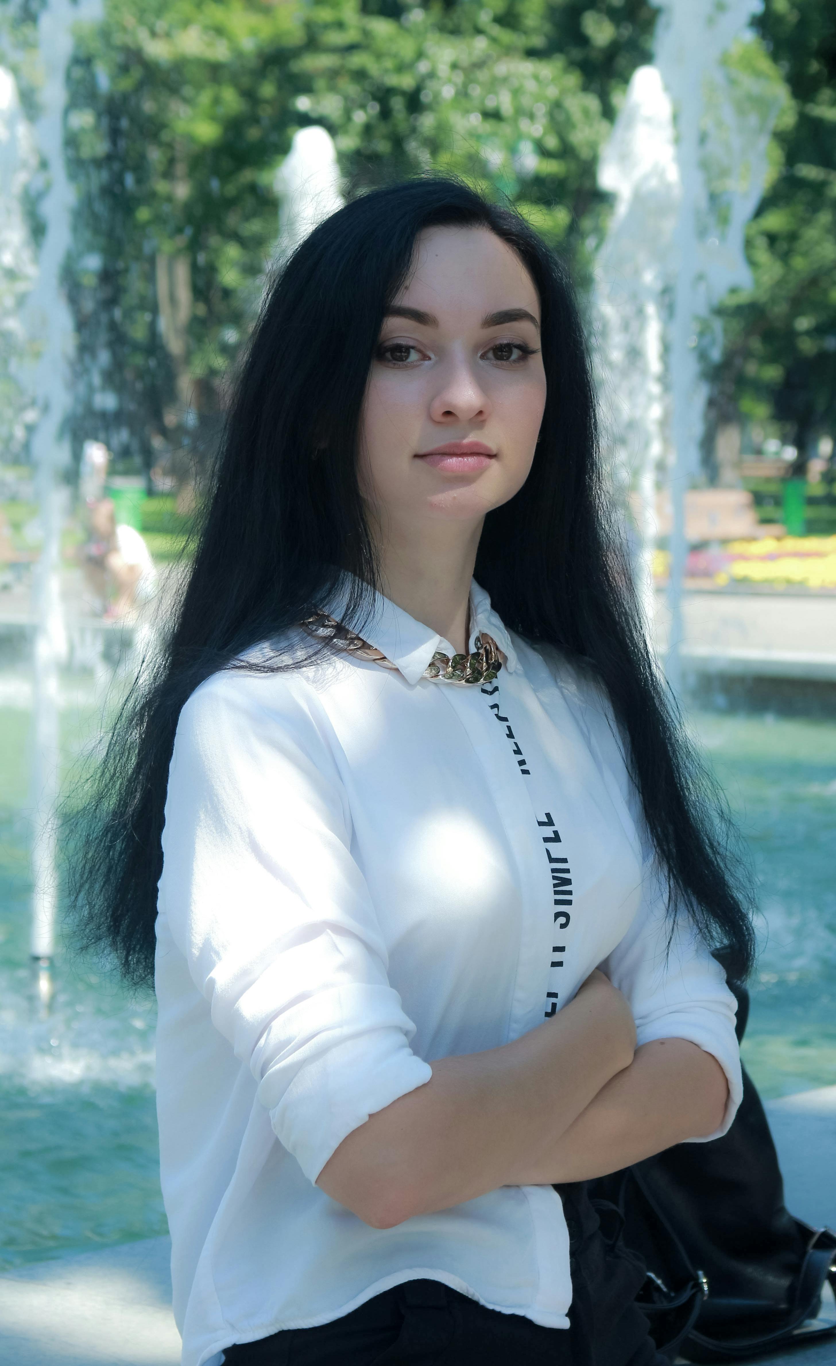 Gratis Ung kvinne står selvsikkert ved en parkfontene om sommeren. Arkivbilde