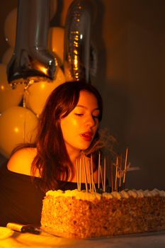 Young woman blowing out candles on a birthday cake during a celebration with balloons.
