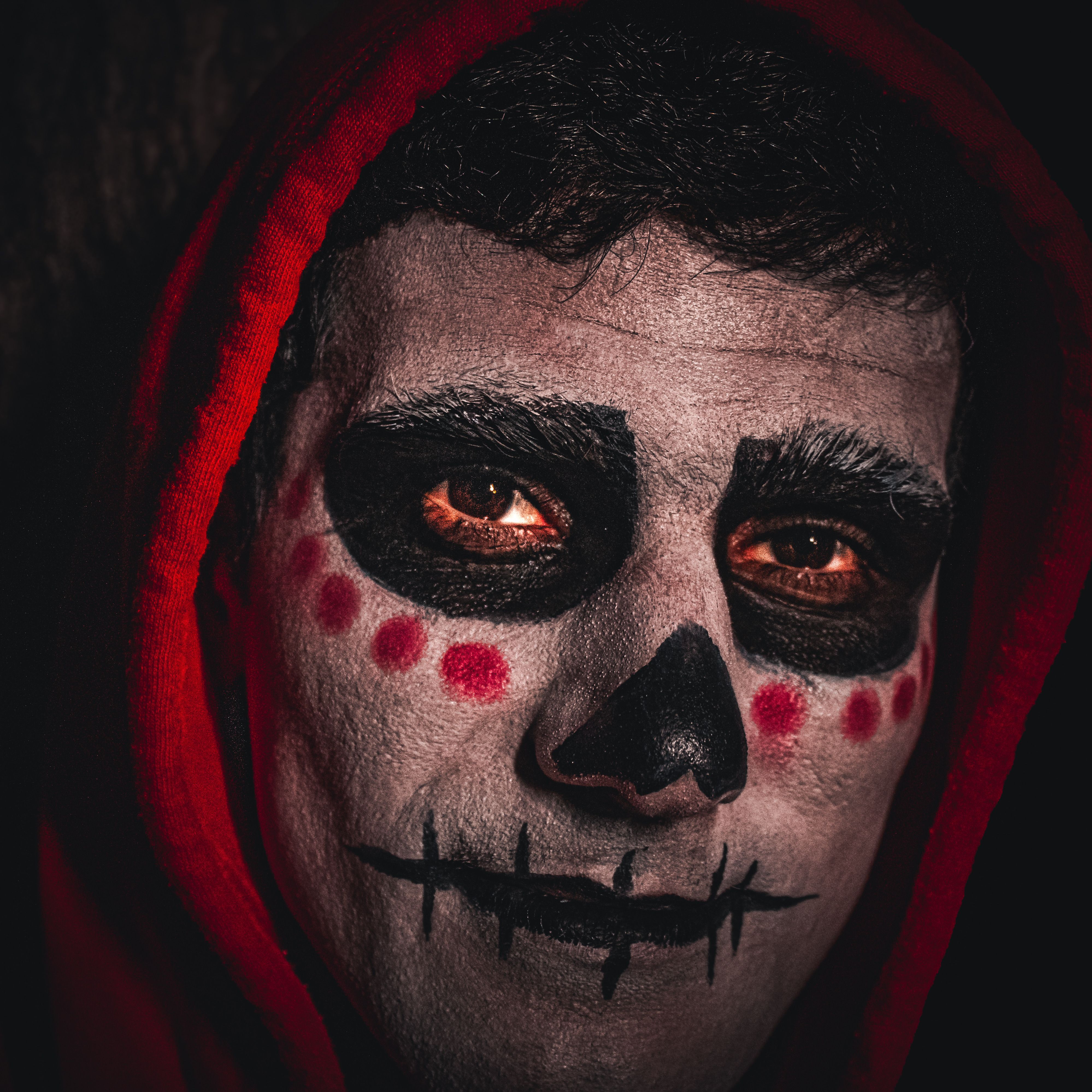 Close-up portrait of a person with traditional Day of the Dead face paint and red hood.