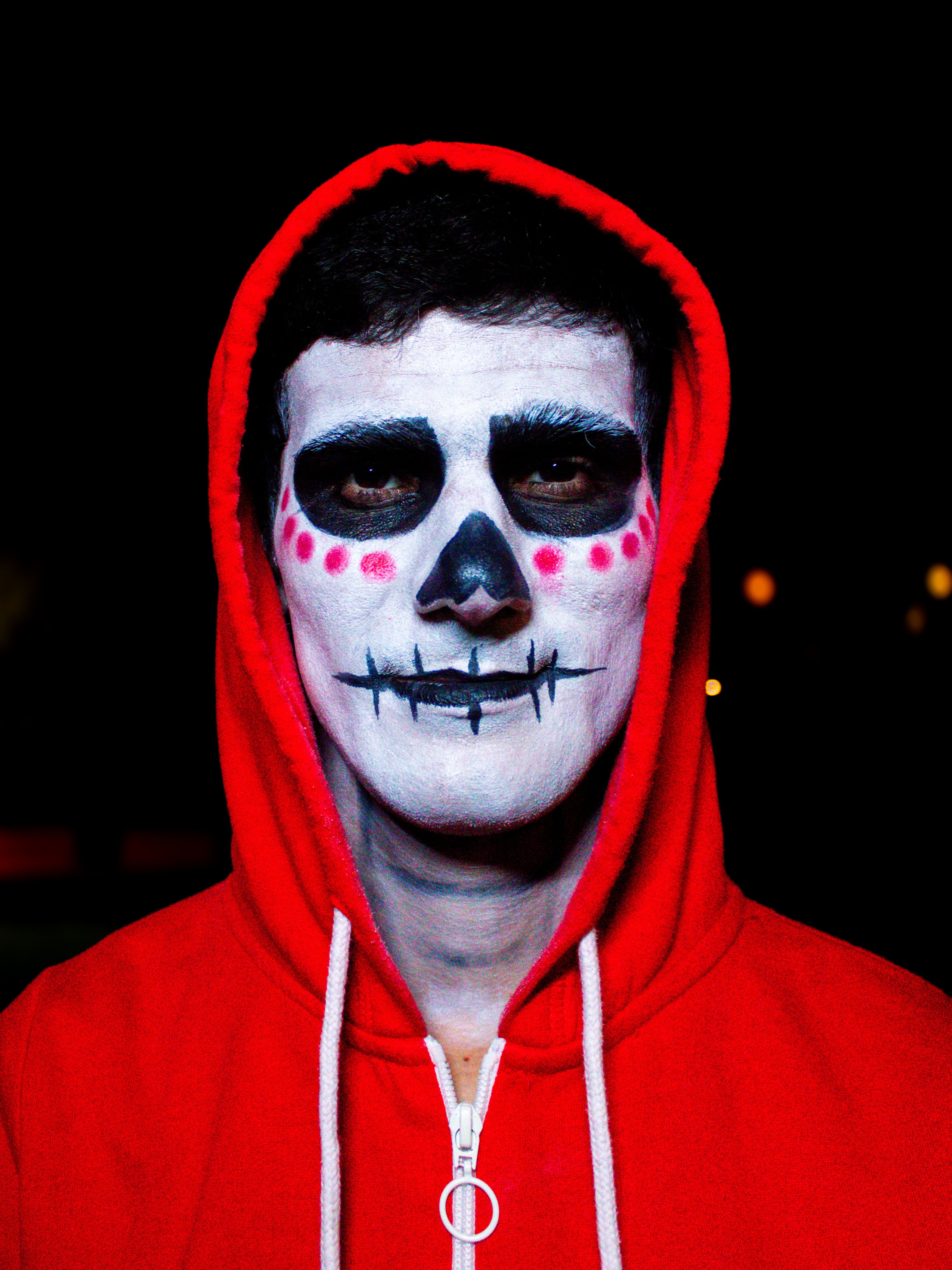 Teenager wearing skull face paint and red hoodie at night.
