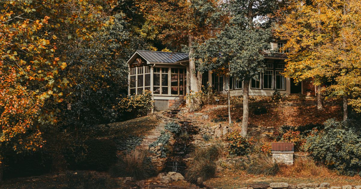 Beautiful fall scene of a cozy cottage surrounded by colorful autumn trees by a tranquil lake.