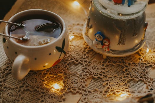 Warm holiday scene with tea, lace, and snow globe, creating a cozy winter ambiance.