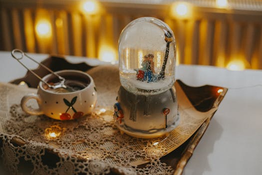 Warm and cozy winter scene featuring a snow globe and a cup of tea with festive decor.