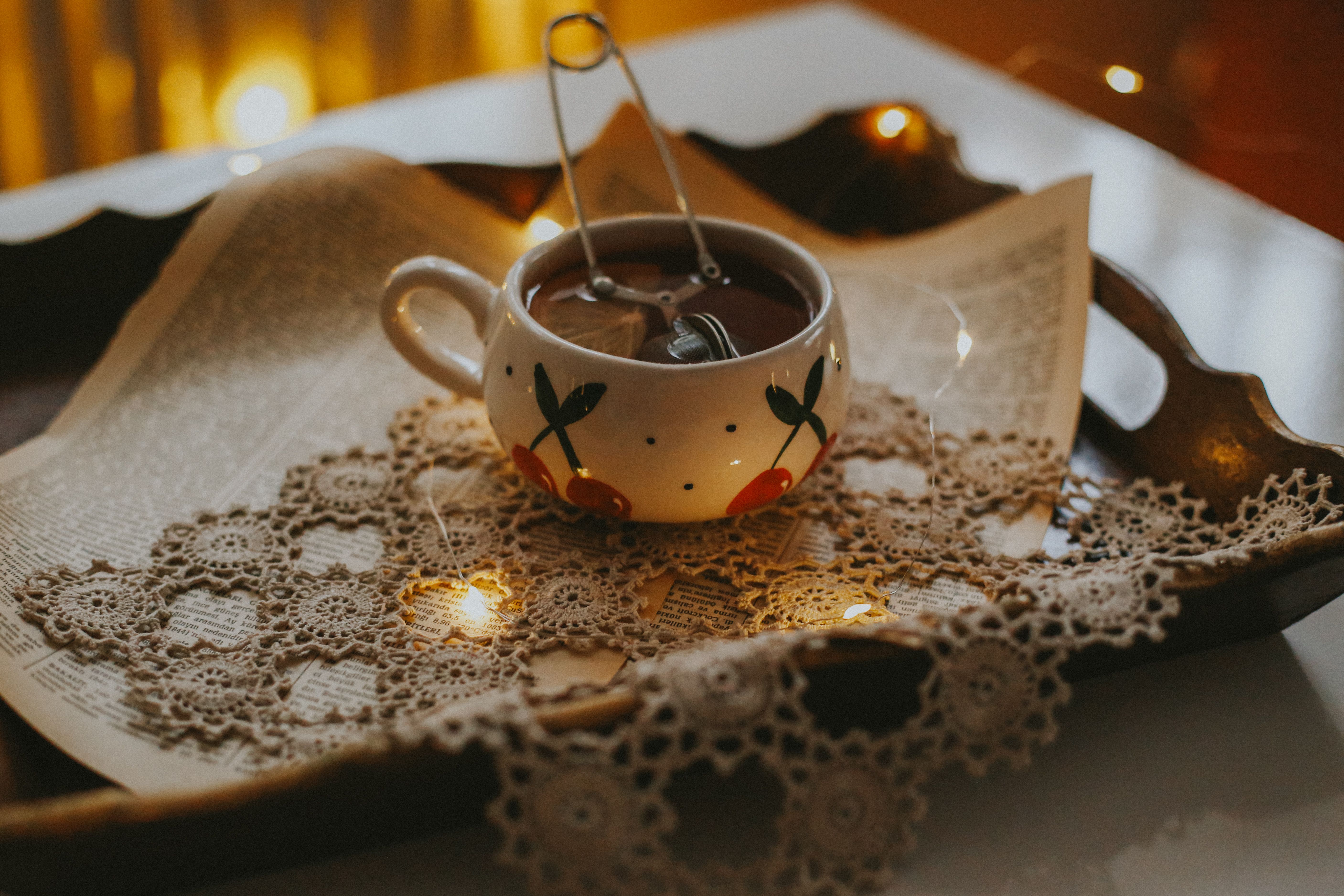 Warm and cozy tea setup with lace, book pages, and ambient string lights in a relaxing indoor scene.