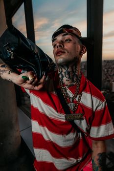 Tattooed man in striped shirt poses with bag in Buenos Aires at sunset.