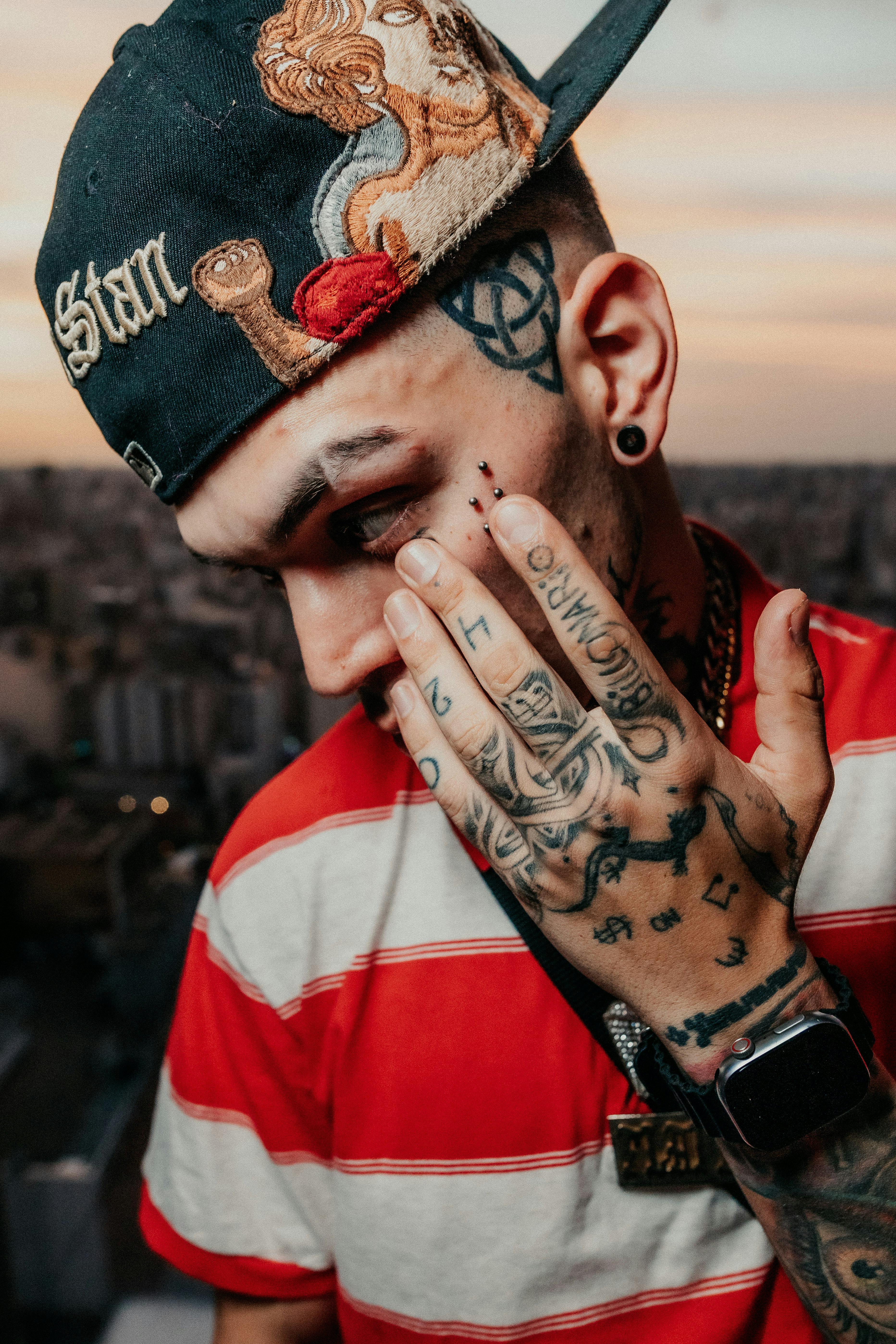 A tattooed adult in a striped shirt with the cityscape of Buenos Aires at sunset. Urban style and expression.