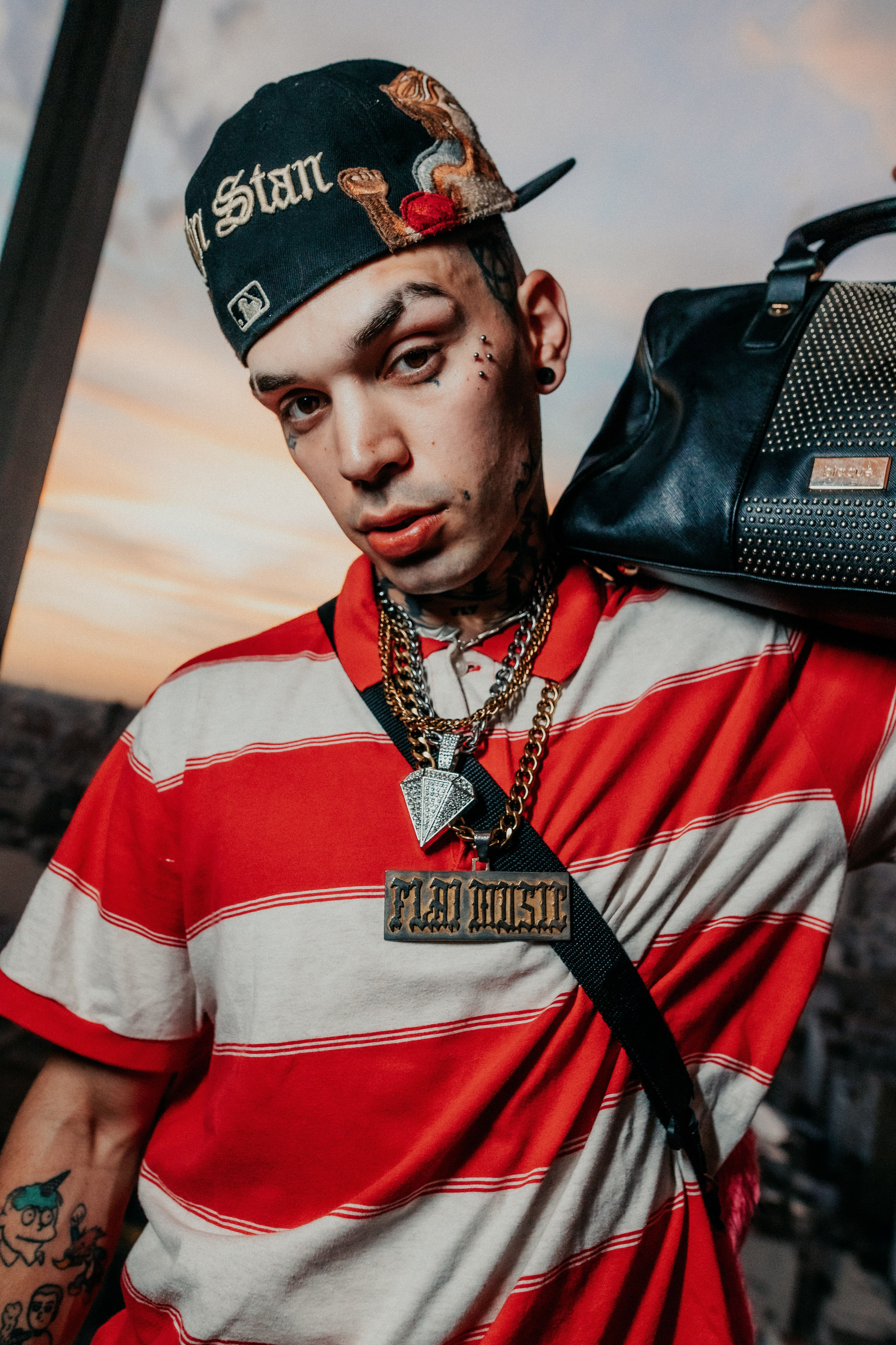 Young man in a stylish outfit poses with a bag at sunset in Buenos Aires.