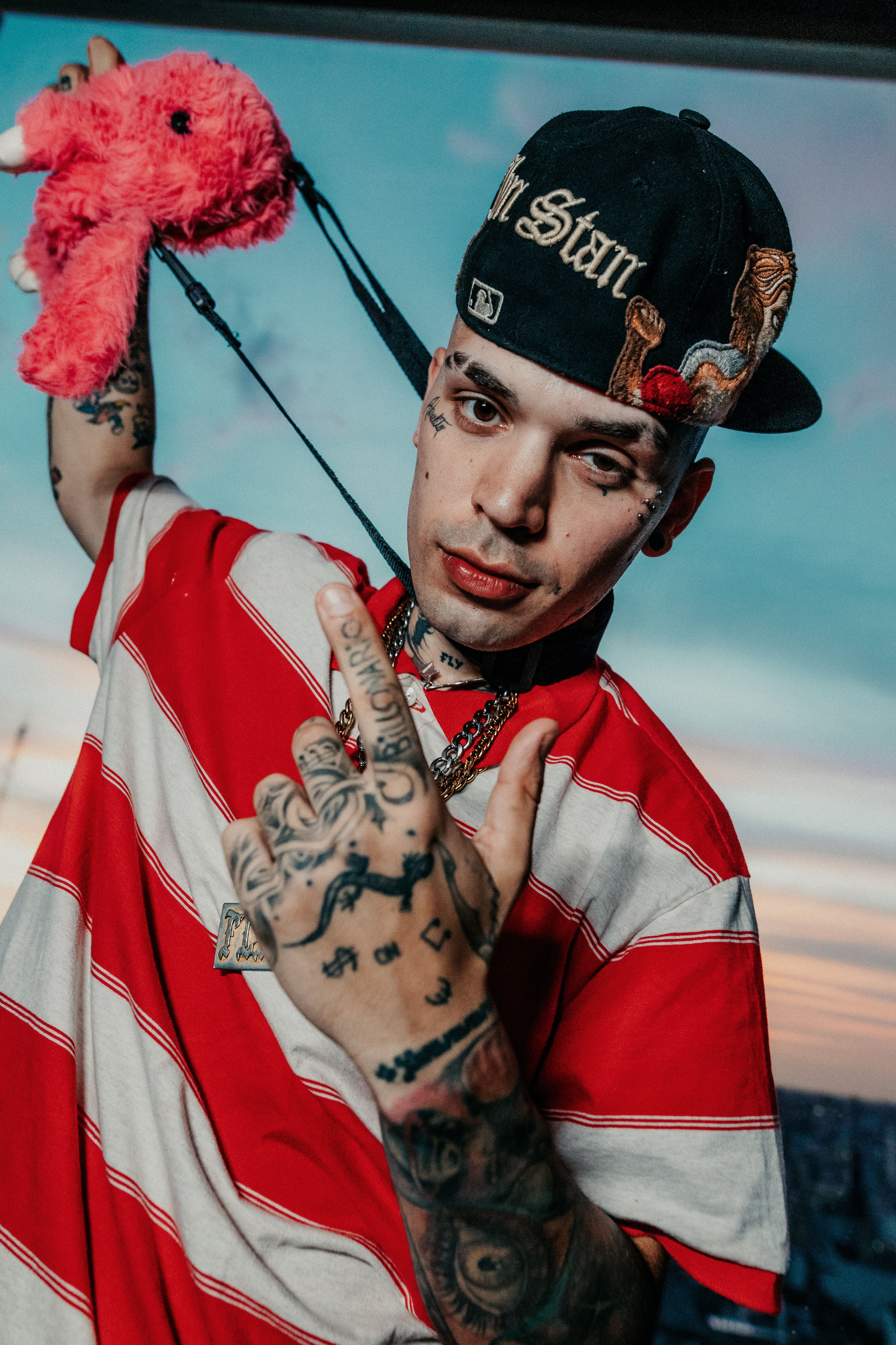 Young man with tattoos and streetwear posing with plush toy in Buenos Aires.