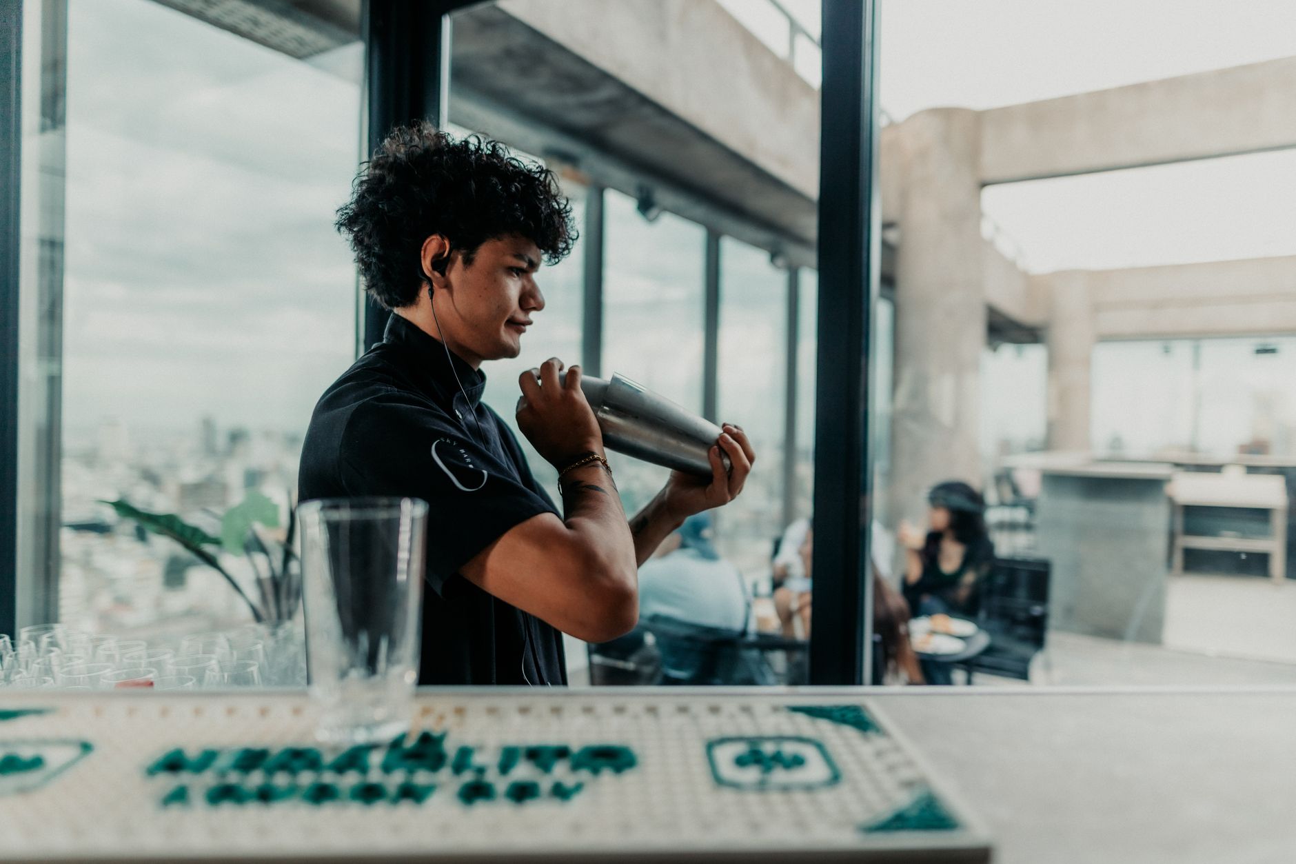 Bartender skillfully shaking a cocktail shaker on a rooftop bar in Buenos Aires with a view of the city.
