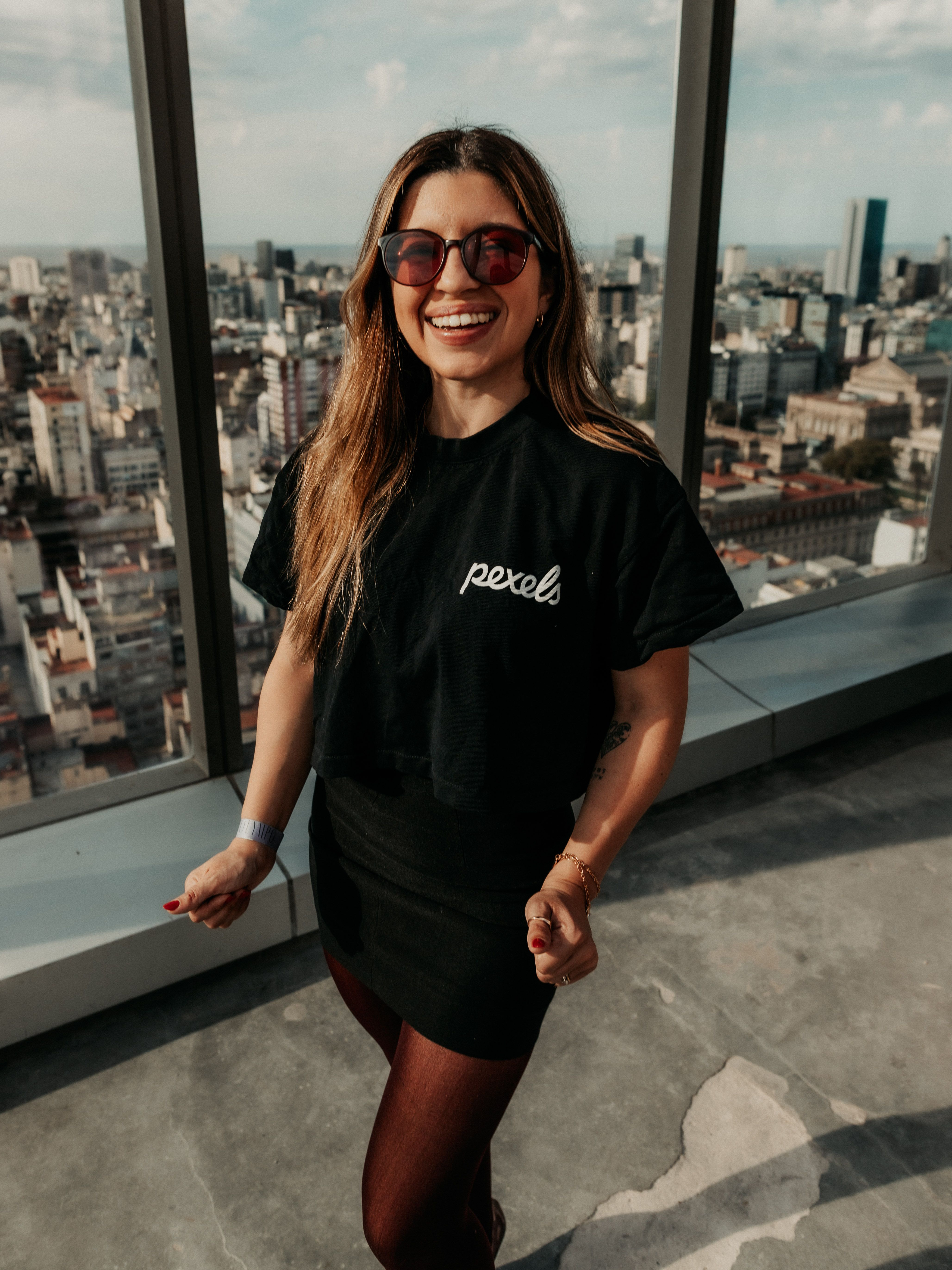 A smiling woman in sunglasses enjoys a panoramic view of Buenos Aires from a high-rise building.