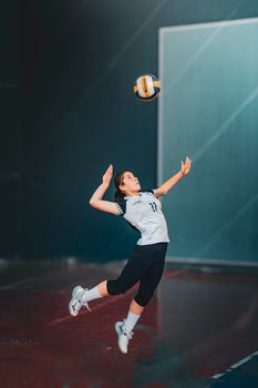 Young female athlete serving in volleyball match indoors, showcasing skill.
