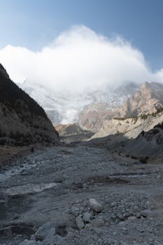 Majestic alpine landscape with a glacial valley under a cloud-covered peak.