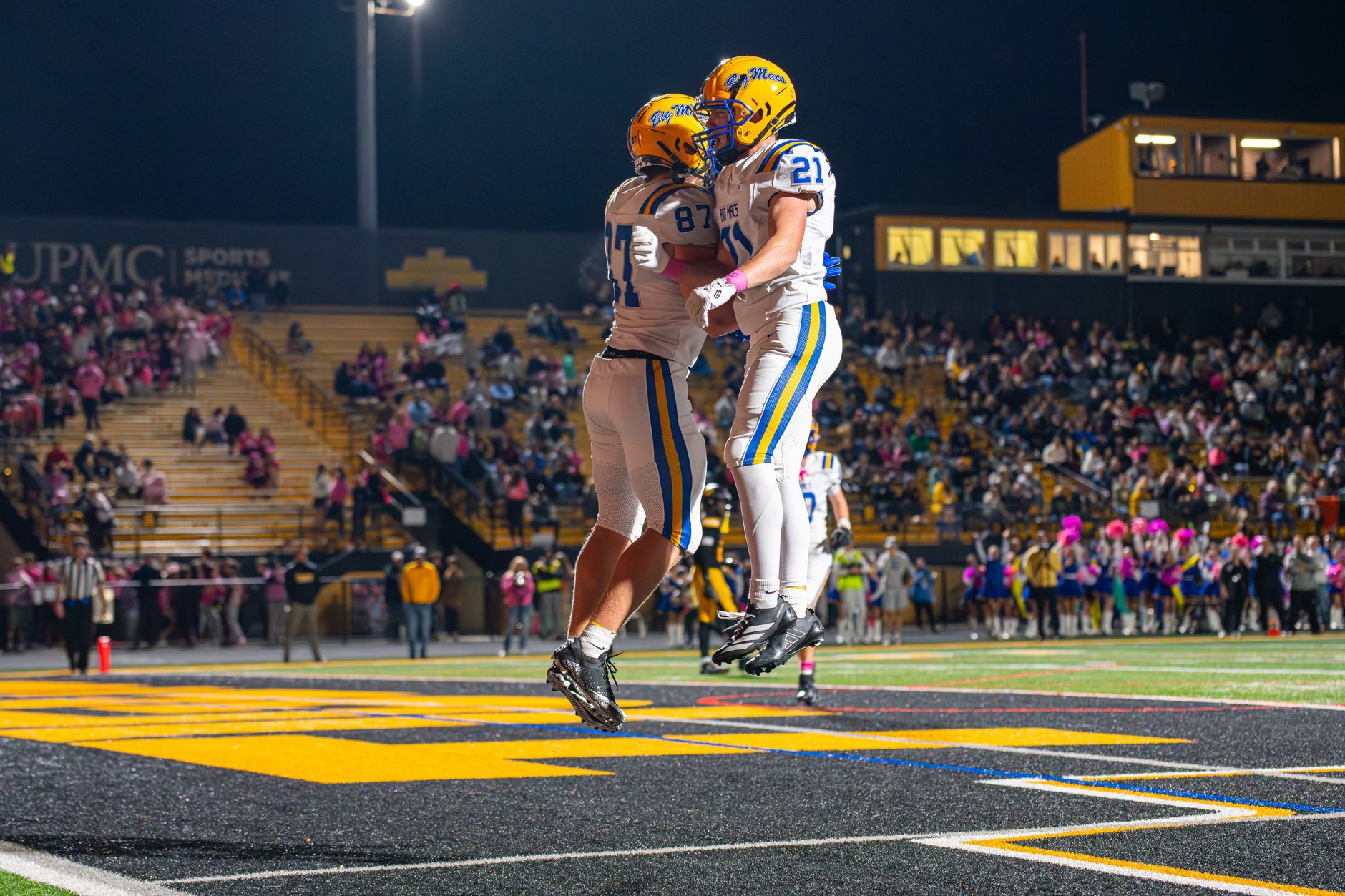 Football players celebrating during a thrilling nighttime game at a packed stadium.