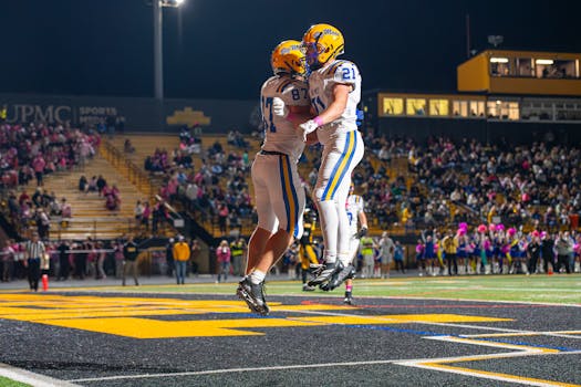 Football players celebrating during a thrilling nighttime game at a packed stadium.