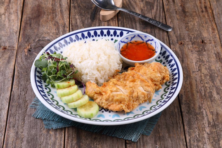 Crispy chicken served with rice, cucumber salad, and dipping sauce on a rustic wooden table.