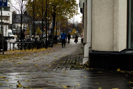 City street with people walking on a wet autumn day, fallen leaves.