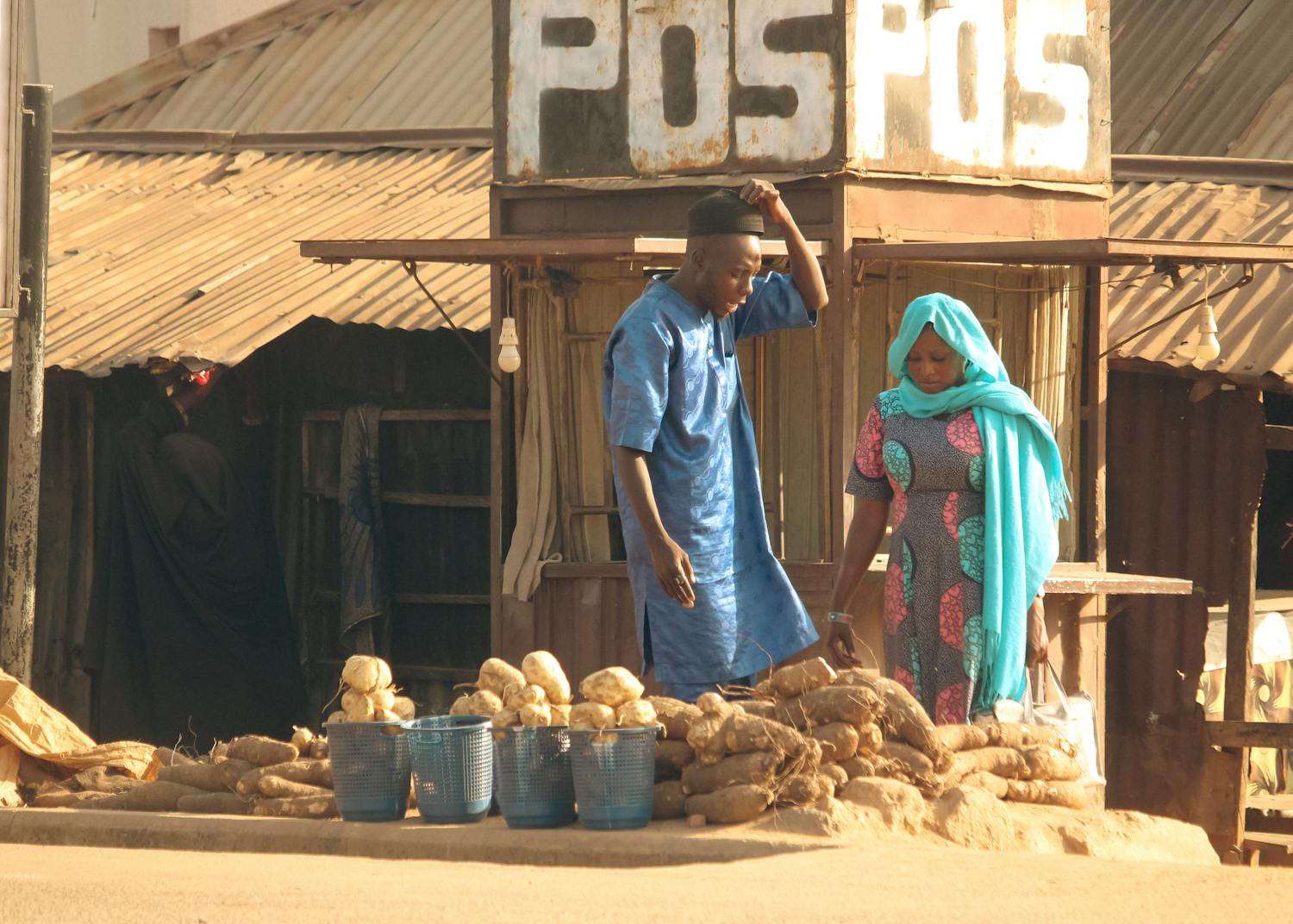 A man and woman selling yams at an outdoor market stall