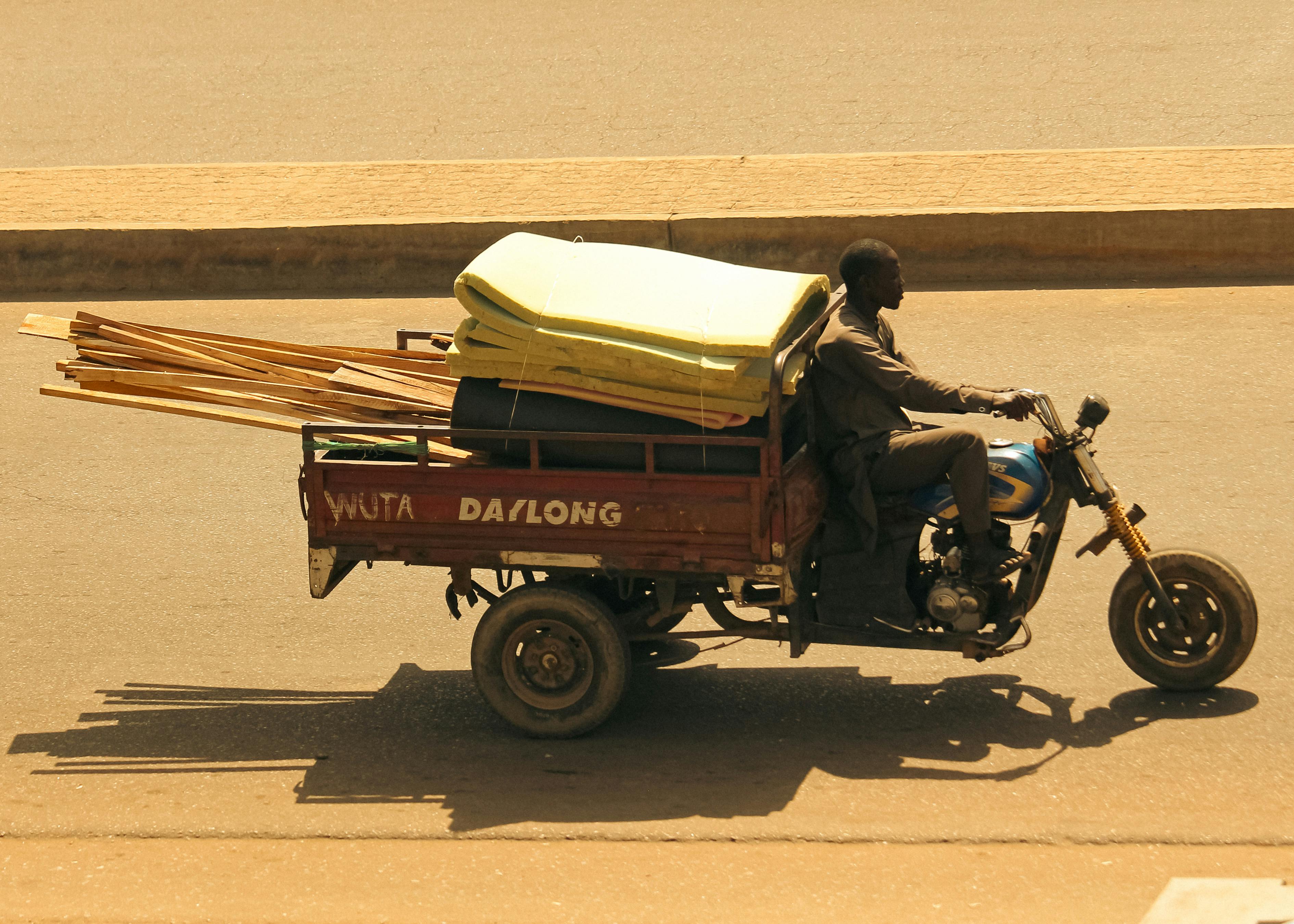 A man rides a tricycle transporting goods on a sunny day, highlighting local transportation.