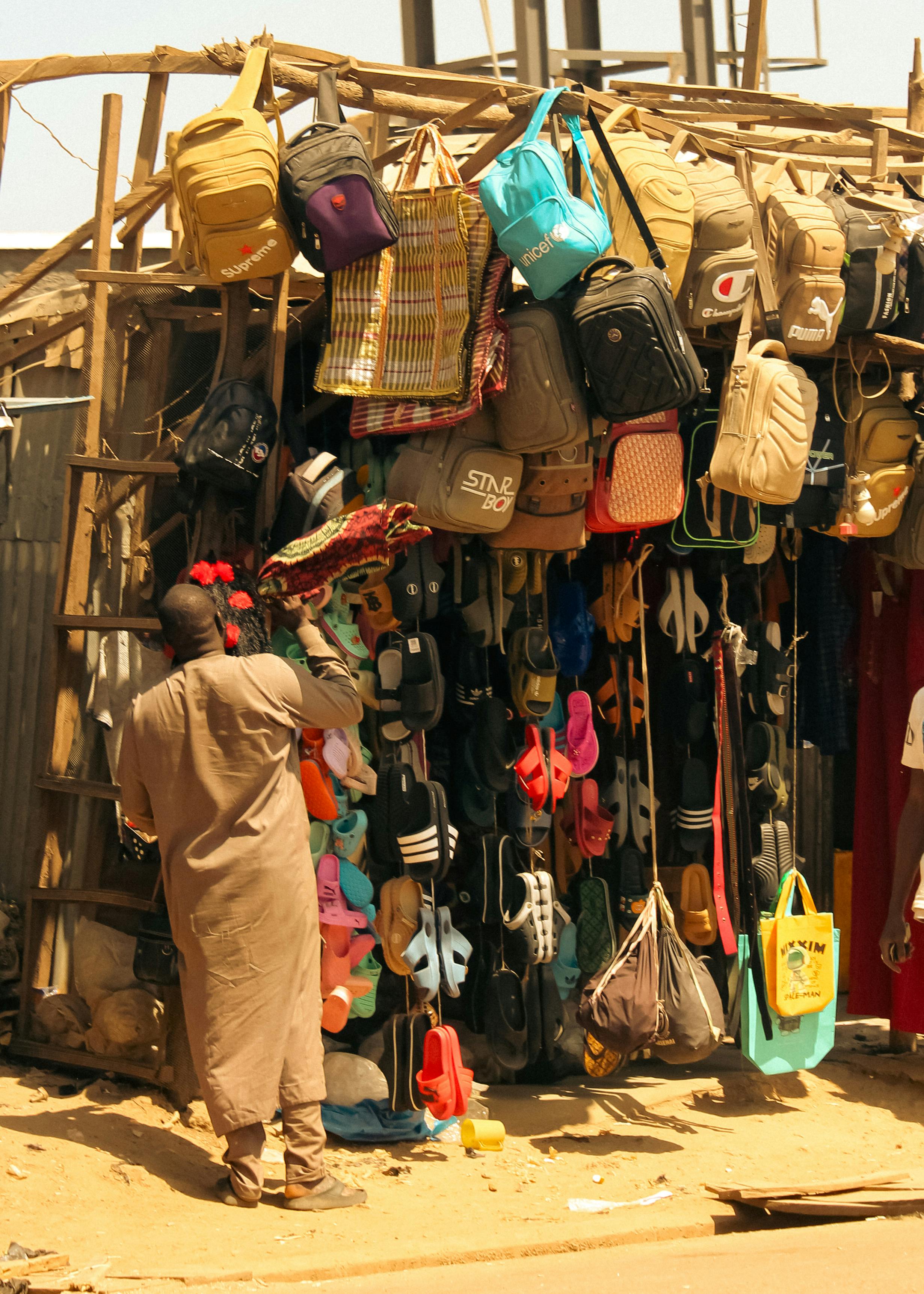 A vibrant outdoor market stall displaying various bags, footwear, and accessories under the sun.