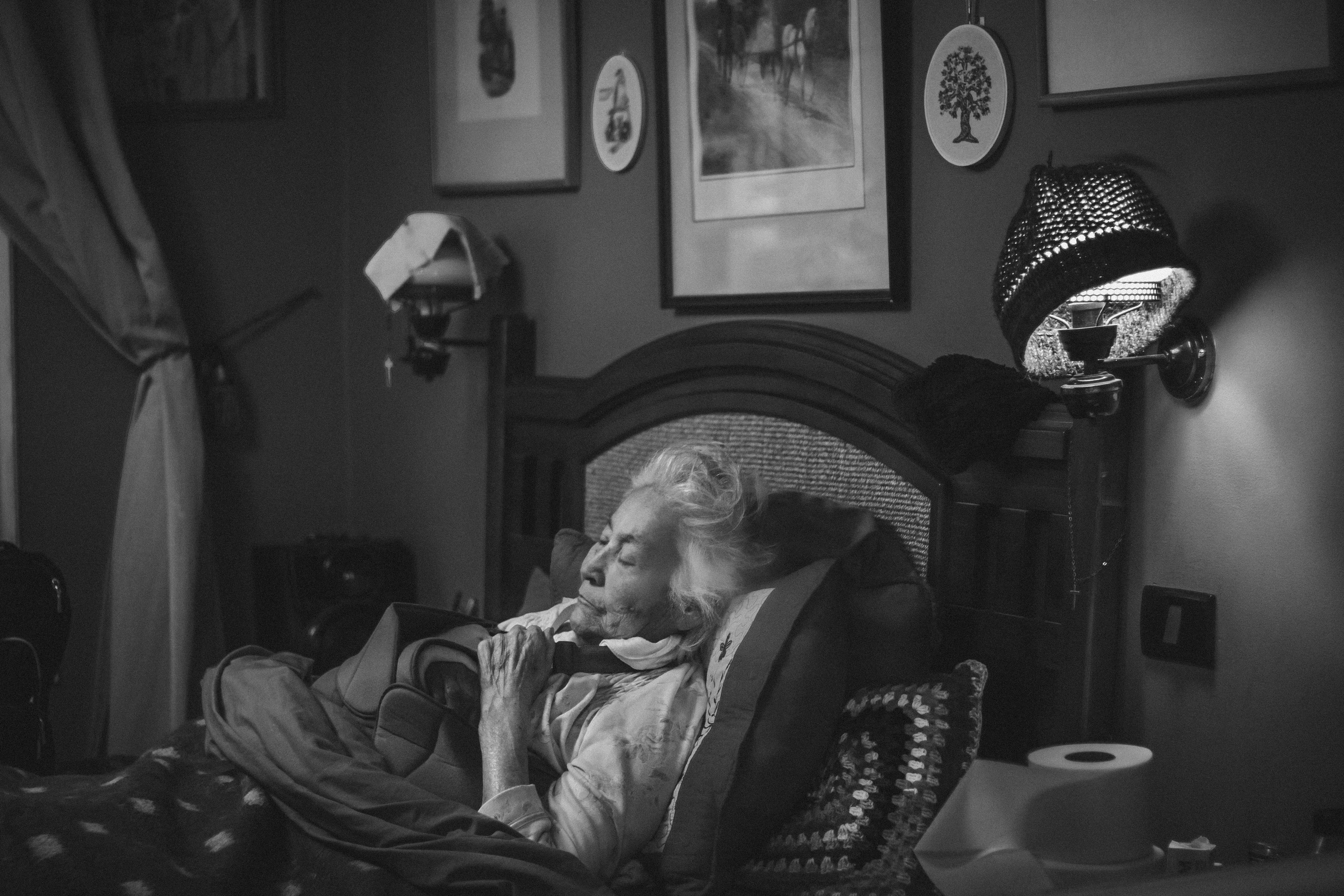 Black and white photo of a senior woman resting peacefully in a cozy bedroom.