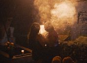 Two people perform a mystical evening ritual with candlelight and smoke outdoors.