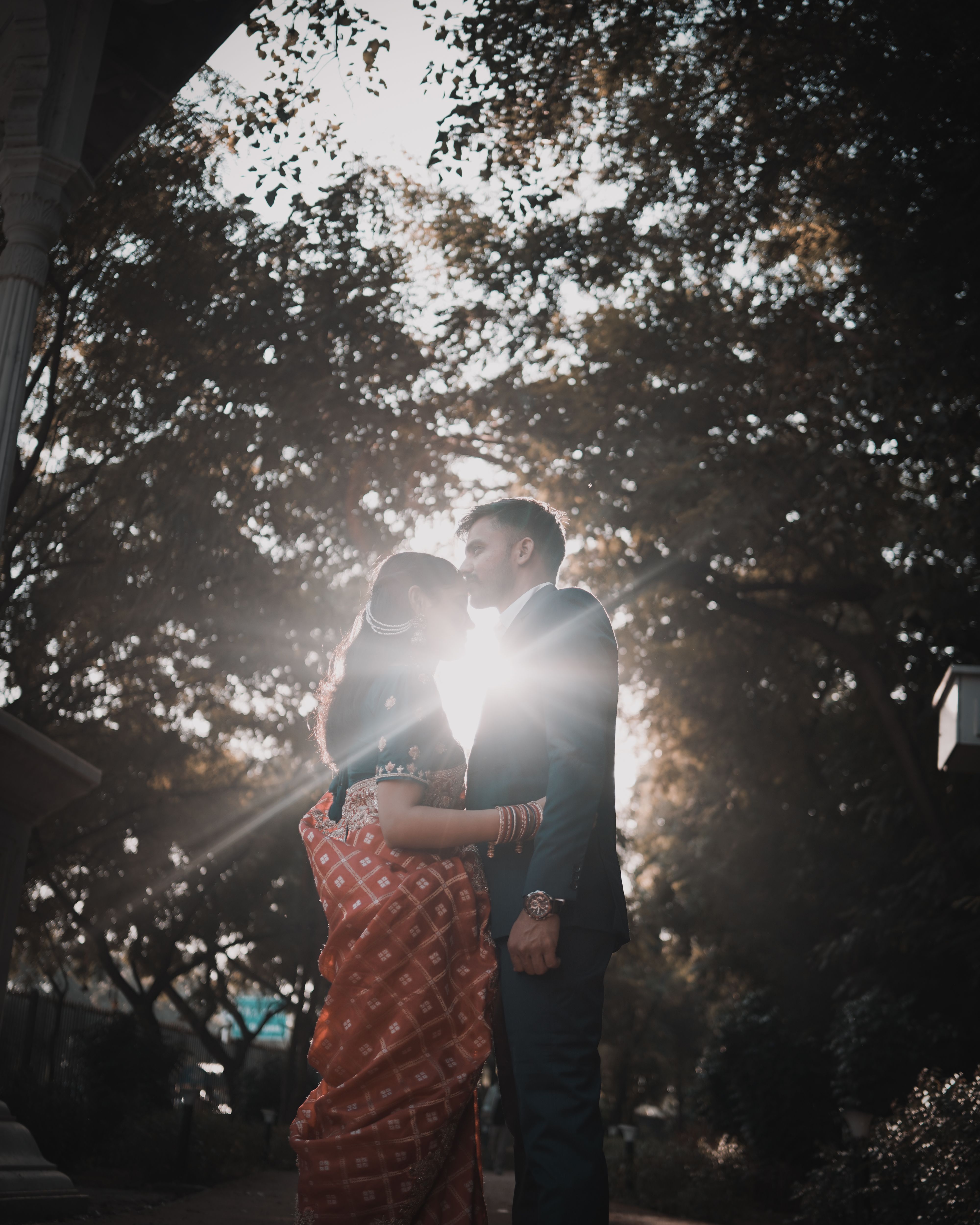 A couple in traditional attire sharing a romantic moment outdoors during sunset.