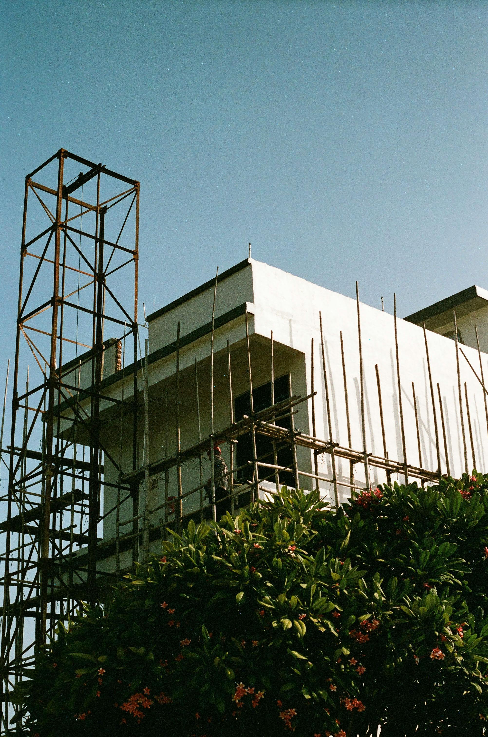 A partially constructed white building with scaffolding and a clear blue sky backdrop.