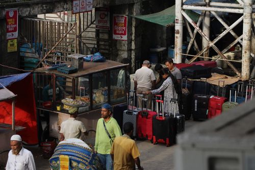 Free Travelers with luggage at a bustling outdoor market scene. Stock Photo