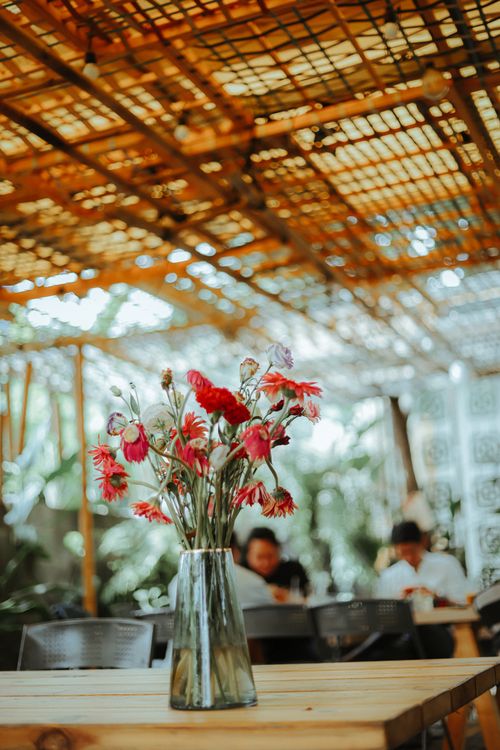Free Vibrant pink flowers in a vase on a wooden table in a stylish outdoor cafe. Stock Photo