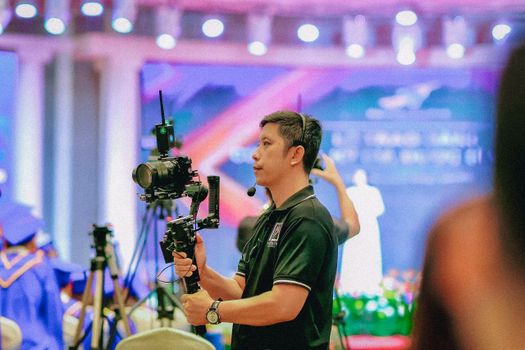 Professional videographer using gimbal at a colorful graduation event indoors.