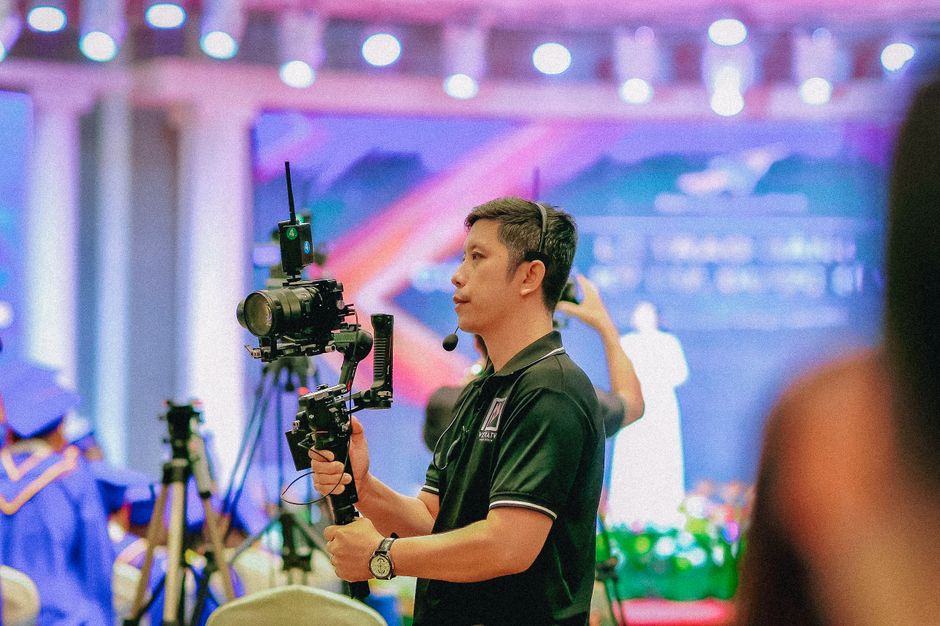 Professional videographer using gimbal at a colorful graduation event indoors.